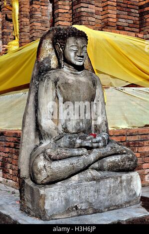 Lamphun, Thailand:  A stone Buddha figure seated in Lotus position at the base of the Suwanna Chedi at a Thai temple Stock Photo