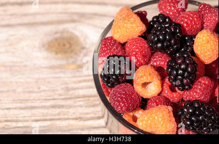 Organic golden and red raspberries mixed with blackberries in a glass bowl on a rustic farm table. Stock Photo