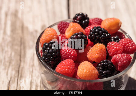Organic golden and red raspberries mixed with blackberries in a glass bowl on a rustic farm table. Stock Photo