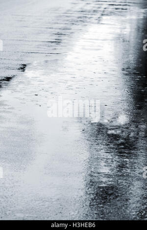 grey asphalt with rain puddles and rain drops falling on it. street in autumn. Stock Photo