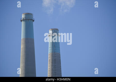 Upper portion of two stacks of a power plant producing smoke, against a blue, cloudless sky Stock Photo