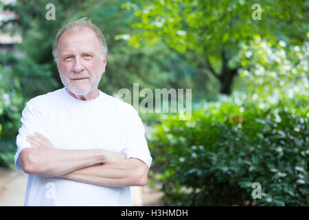 Closeup portrait of happy, confident, cheerful, smiling senior mature man, arms folded crossed, isolated outside outdoors Stock Photo