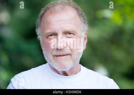 Closeup headshot portrait of happy, confident, cheerful, smiling senior mature man, isolated green trees foliage background. Stock Photo