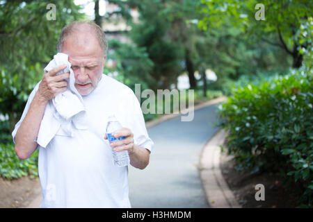 Closeup portrait, old gentleman in white shirt having difficulties with extreme heat, high temperature, wiping sweat from face, Stock Photo