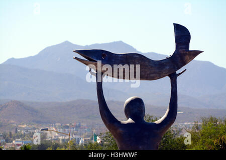 Close-Up Statue of a Man Holding a Fish Towards the Sun Heavens at Wirikuta Botanical Garden, Mexico with Mountains &  Blue Sky Stock Photo