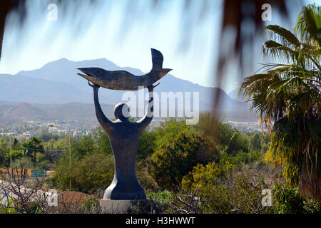 Statue of a Man Holding a Fish Towards the Heavens at Wirikuta Botanical Garden, Baja, Cabo, Mexico with Mountains and Blue Sky Stock Photo