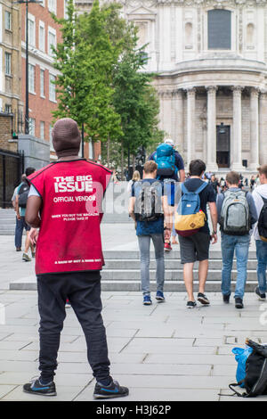The Big Issue magazine official vendor in a red tabard outside St Paul's Cathedral, City of London, UK Stock Photo