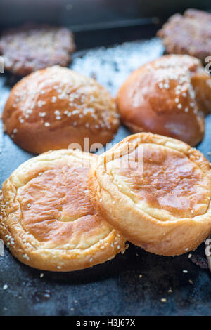 seeded burger buns and burgers on a black heated surface being cooked and warmed up in a food truck Stock Photo