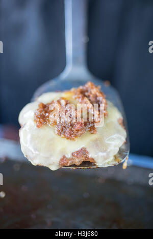 cheeseburger topped with pulled pork on a silver metal spatula above a heated surface used to cook burgers in a food truck Stock Photo
