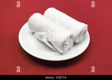Close focus on white rolled napkin made from rough cotton inside white dish on red fabric table Stock Photo