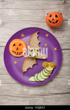 Halloween bat and snake made of bread and cucumber on plate and board Stock Photo