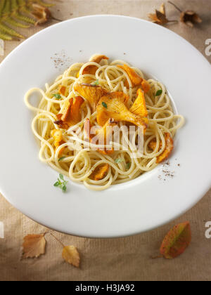 Wiild organic chanterelle or girolle Mushrooms (Cantharellus cibarius) or sauteed in butter and hebs with spaghetti Stock Photo