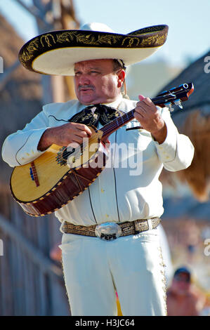 Mariachi Guitar Player Performs on Sunny Beach during Wedding wearing a Sombrero Hat & White Suite with Gold Bucket in Mexico Stock Photo