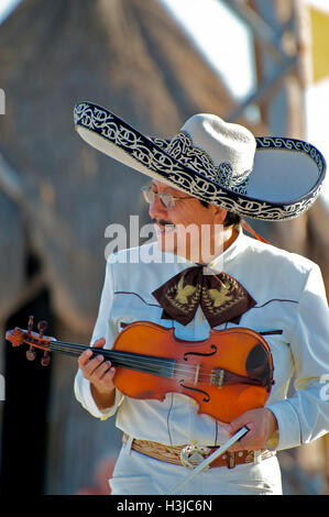 Mariachi Violin Player Performs on Sunny Beach during Wedding wearing a Sombrero Hat & White Suit with Gold Bucket in Mexico Stock Photo