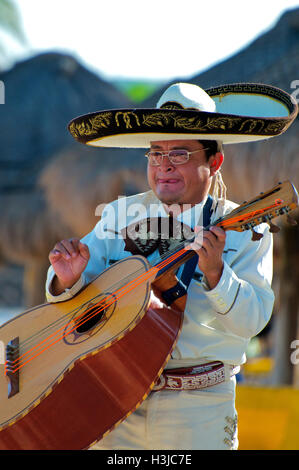 Mariachi Guitar Player Performs on Sunny Beach during Wedding wearing a Sombrero Hat & White Suit with Gold Bucket in Mexico Stock Photo