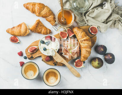 Breakfast with croissants, homemade ricotta cheese, figs, fresh berries, prosciutto, honey and espresso coffee on rustic serving Stock Photo