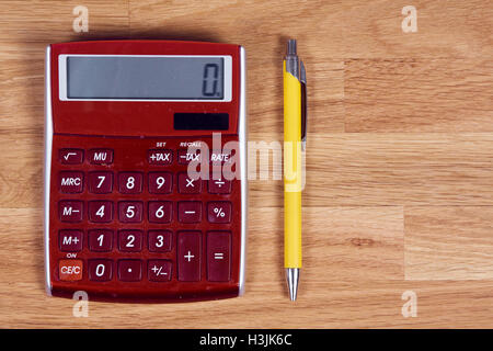 Red calculator and yellow pen on a wooden oak table Stock Photo