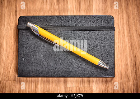 Closed notebook and yellow pen ballpoint on a brown wooden table Stock Photo