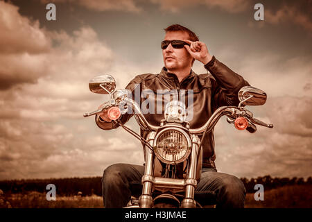 Biker man wearing a leather jacket and sunglasses sitting on his motorcycle. Filter applied in post-production. Stock Photo