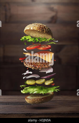 Classic burger ingredients flying on a wooden brown background Stock Photo