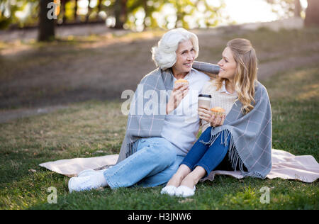 Two cheerful smiling women sitting on the ground and talking. Stock Photo