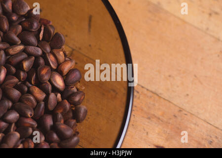 Pine nuts in shells of ciberian cedar as a background in glass bowl on wooden floor. Copyspace Stock Photo