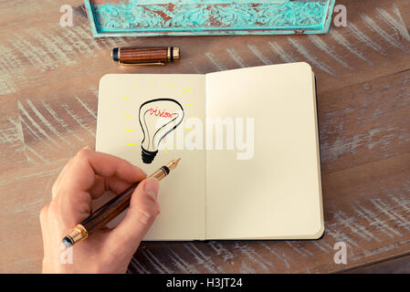 Retro effect and toned image of a woman drawing a lighting bulb with fountain pen on a notebook. VISION symbol and concept Stock Photo