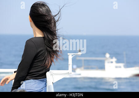 Back view of young asian woman with waving long hair looking at the sea from the deck of cruise ship Stock Photo