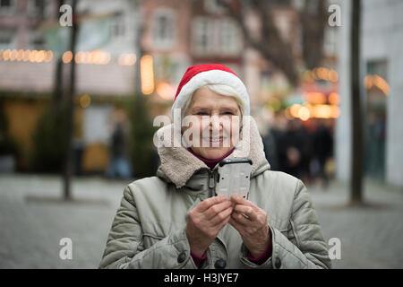 Elderly woman wearing red hat and using smartphone at Christmas market in Aachen, Germany Stock Photo