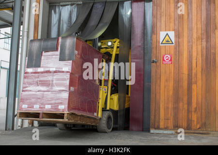 Forklift driver with pallets driving through doorway of packaging factory Stock Photo