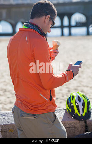 Bournemouth, Dorset, UK. 9th Oct, 2016. Man eating an ice cream whilst checking mobile phone at Bournemouth beach on a glorious warm sunny day  Credit:  Carolyn Jenkins/Alamy Live News Stock Photo