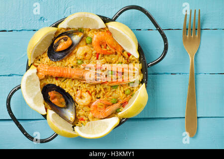 Spanish paella on a blue wooden table with fresh lemon and a golden fork Stock Photo