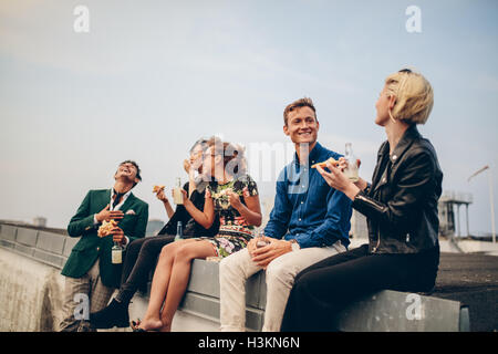 Group of friends partying on terrace, drinking and eating. Young men and women enjoying drinks on rooftop. Stock Photo