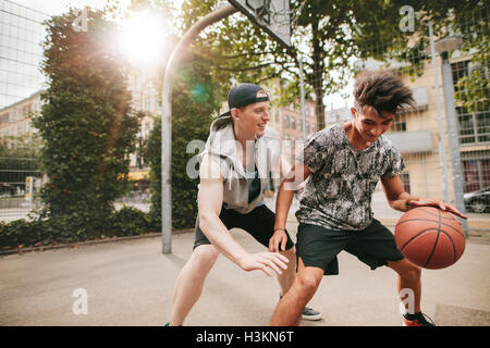 Two young friends playing basketball on court outdoors and having fun. Streetball players having a basketball game. Stock Photo