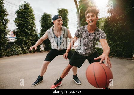 Two young friends playing basketball and having fun. Streetball players having a game of basketball on court outdoors. Stock Photo