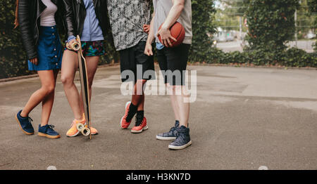 Cropped shot of group of people standing together with basketball and skateboard. Low angle shot with focus on men and women leg Stock Photo