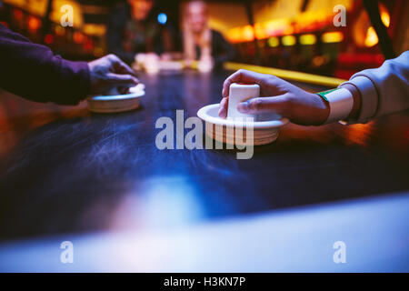 Hands of young people holding striker on air hockey table. Friends playing air hockey. Stock Photo