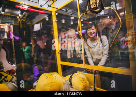 Happy young woman playing toy grabbing game with friends at amusement park. Stock Photo