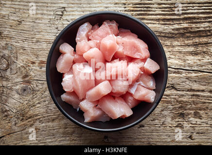 Raw cut meat chunks in black bowl on wooden table, top view Stock Photo