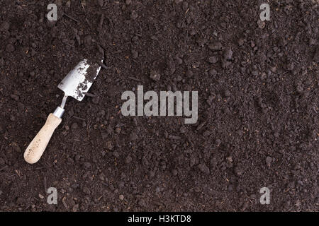 A single white spade lies in rich black soil as seen from an overhead view Stock Photo