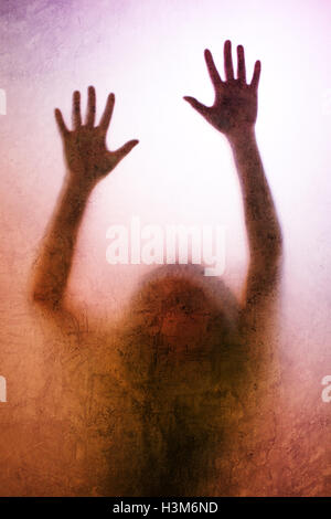 Trapped woman concept with back lit silhouette of hands behind matte glass, useful as illustrative image for human trafficking, Stock Photo