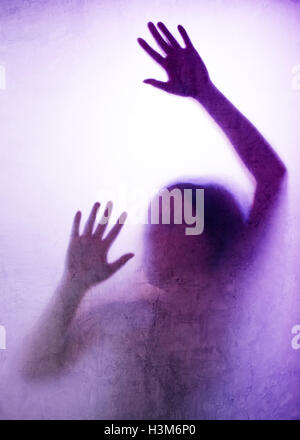 Trapped woman concept with back lit silhouette of hands behind matte glass, useful as illustrative image for human trafficking, Stock Photo