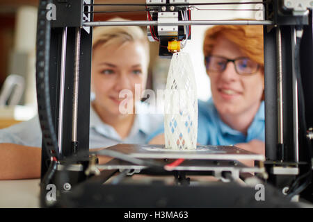 Model of architecture in 3d printer and two designers looking at it Stock Photo