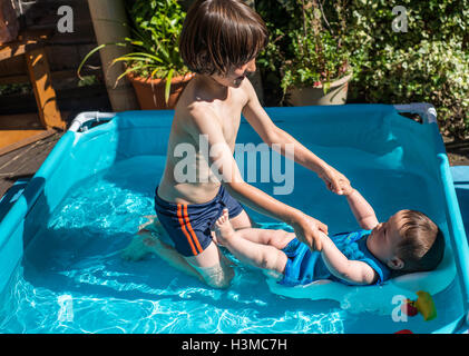 Happy brothers playing in inflatable pool on summer day Stock Photo