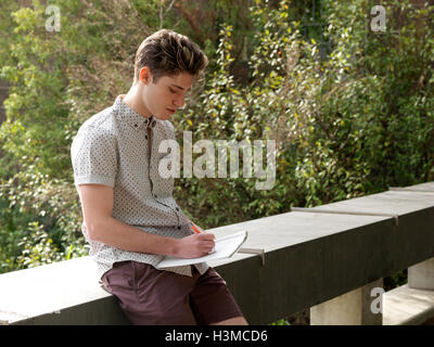 Young man outdoors, writing notes in notepad Stock Photo