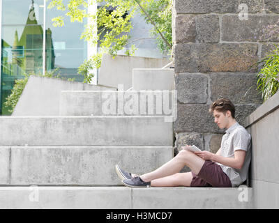 Young man sitting on step, outdoors, writing in notepad Stock Photo
