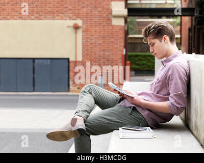 Young man sitting on step, outdoors, reading book Stock Photo