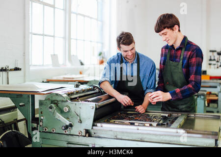 Two young men working on letterpress machine in book arts workshop Stock Photo
