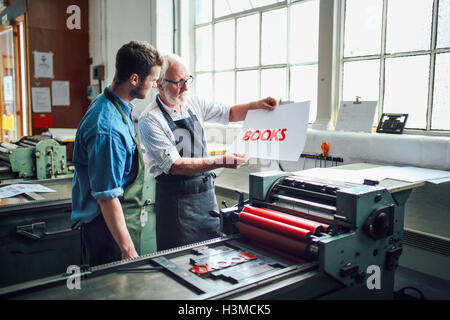 Senior craftsman/technician showing young man letterpress print in book arts workshop Stock Photo