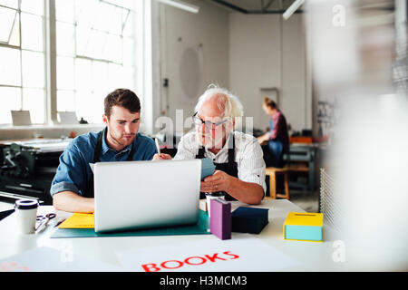 Senior male craftsman and young man looking at laptop in book arts workshop Stock Photo